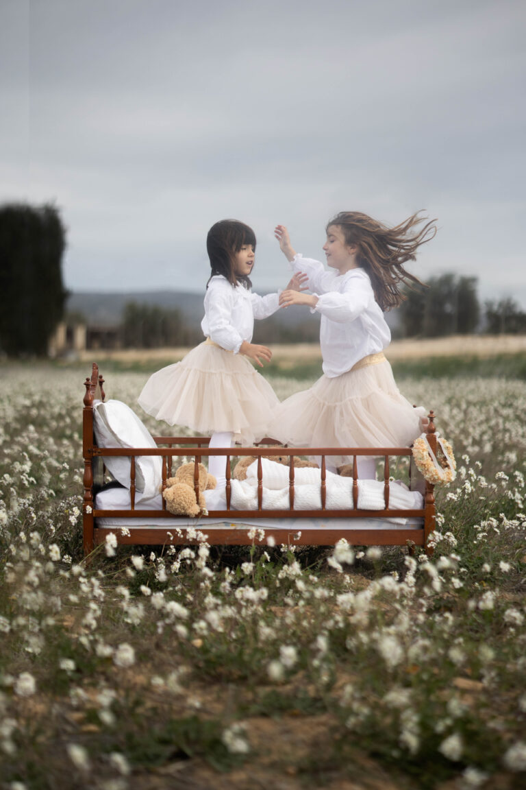 Hermanas disfrutando de una divertida sesión fotográfica mientras saltan sobre una cama rodeada de margaritas en plena naturaleza, Villena